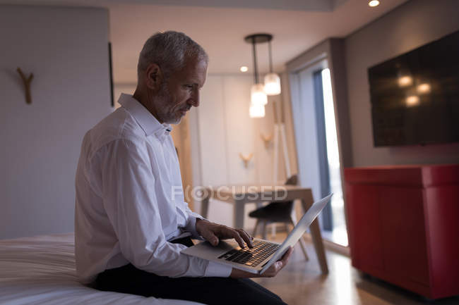 Empresario usando un portátil en la cama en la habitación de hotel - foto de stock