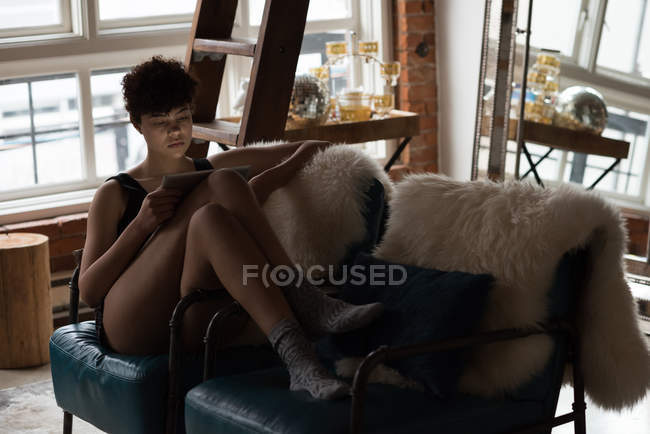 Красива жінка використовує цифровий планшет, розслабляючись на стільці n вітальні — стокове фото