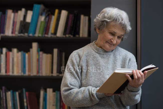 Активная пожилая женщина читает книгу в библиотеке — стоковое фото
