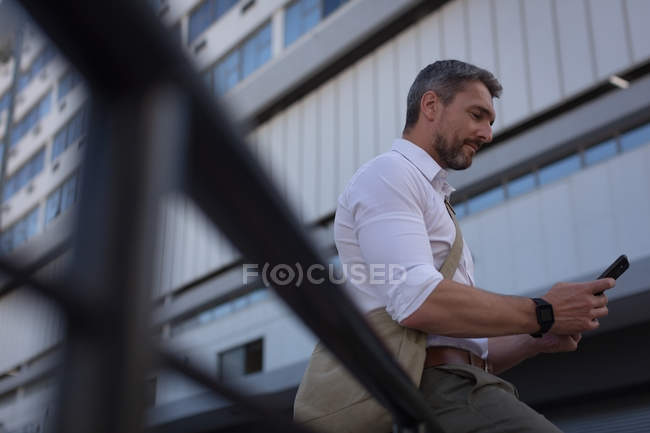 Homme utilisant un téléphone portable près d'un immeuble de bureaux par une journée ensoleillée — Photo de stock