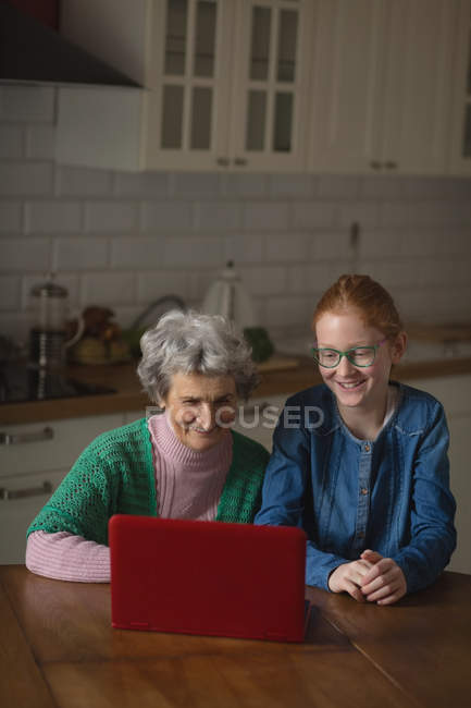 Бабушка и внучка используют ноутбук на кухне дома — стоковое фото