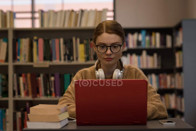 Jovem mulher usando um laptop na biblioteca — Fotografia de Stock