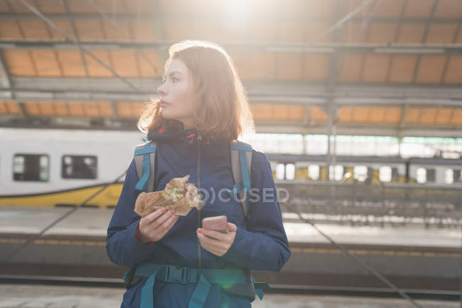 Frau benutzt Handy beim Essen im Bahnhof — Stockfoto