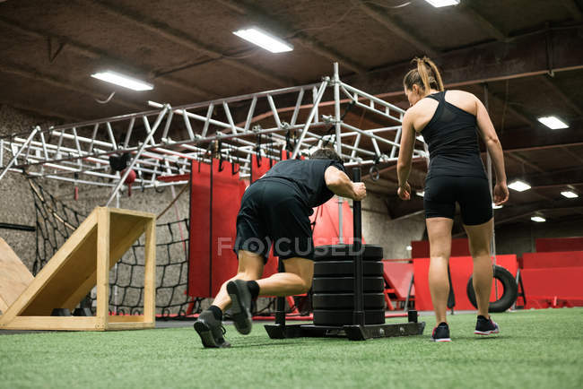 Female trainer helping man with sled pushing in  in fitness studio — Stock Photo