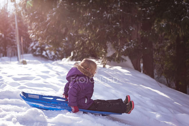 Симпатичная девушка играет в санях зимой. — стоковое фото