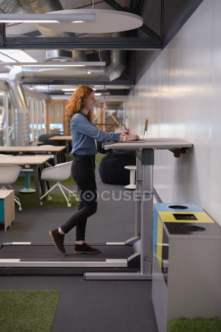Esecutivo femminile che utilizza laptop sul tapis roulant in ufficio — Foto stock