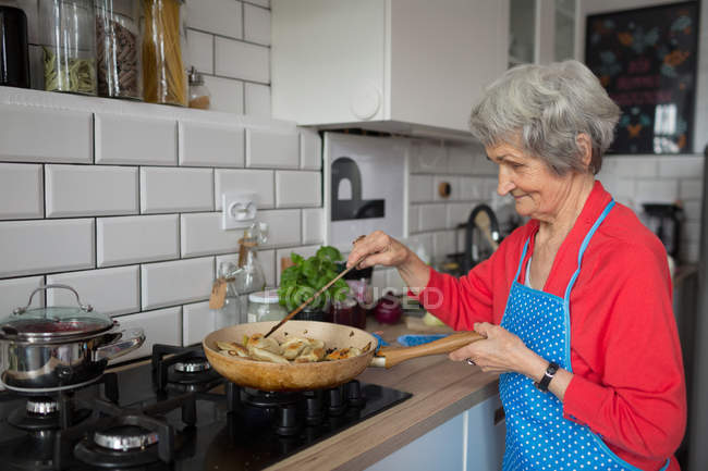 Donna anziana cucina cibo in cucina a casa — Foto stock