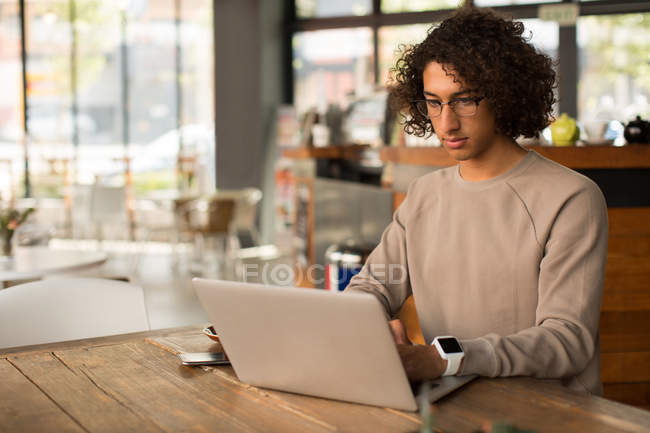 Young man using laptop in cafeteria — Stock Photo
