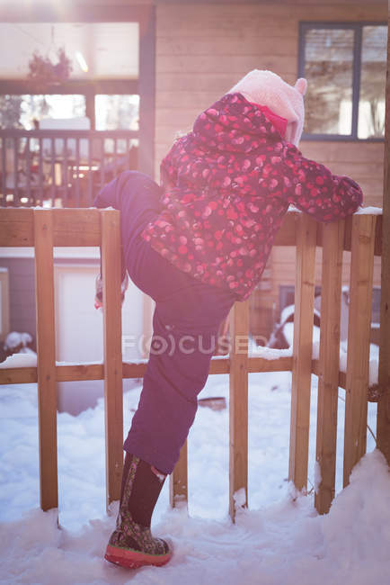 Vista trasera de la niña escalando una valla durante el invierno - foto de stock