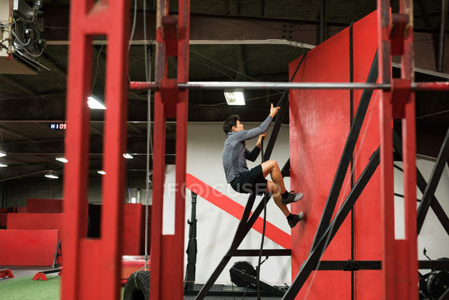 Muskulöser Mann klettert in der Turnhalle an einer Wand mit Seil — Stockfoto