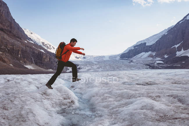 Вид збоку людини, що стрибає через потік взимку — стокове фото