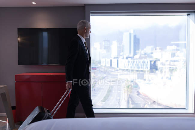Geschäftsmann mit Gepäck schaut im Hotelzimmer aus dem Fenster — Stockfoto