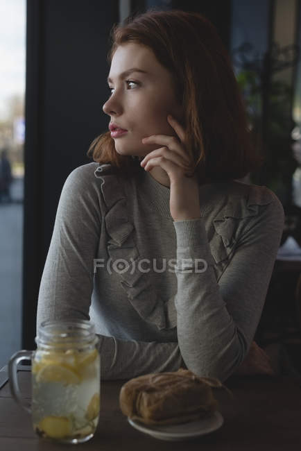 Задумчивая женщина с лимонным чаем и оберточной едой сидит в кафе — стоковое фото
