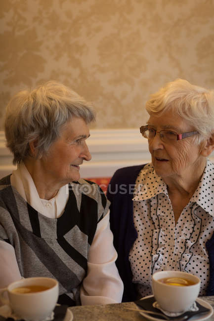 Amigos seniores interagindo uns com os outros enquanto tomam café em casa — Fotografia de Stock