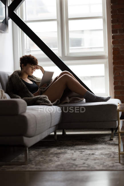Красива жінка використовує цифровий планшет, розслабляючись на дивані вдома — стокове фото