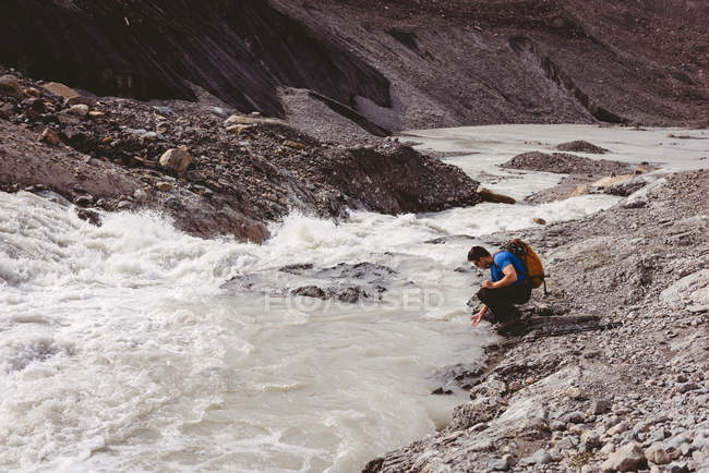 Homme randonneur se laver les mains dans la rivière par une journée ensoleillée — Photo de stock