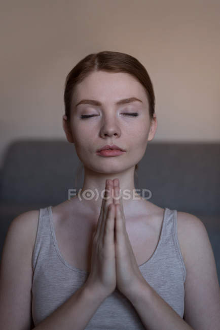 Primer plano de la joven meditando con las manos unidas en la sala de estar - foto de stock