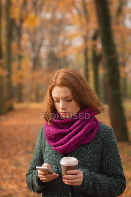 Жінка використовує мобільний телефон, маючи каву в парку — стокове фото