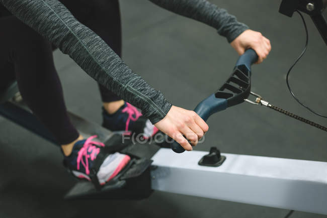 Close up of muscular woman exercising on rowing machine at gym — Stock Photo