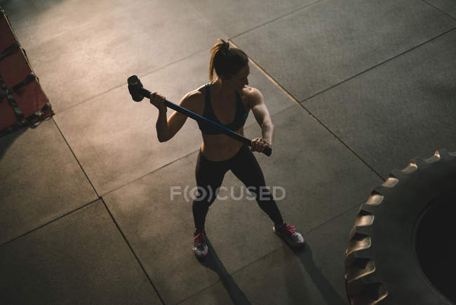 Muscular woman hitting wheel tyre with sledge hammer at the gym — Stock Photo