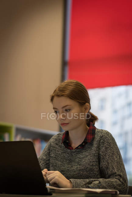 Giovane donna che utilizza un computer portatile in biblioteca — Foto stock