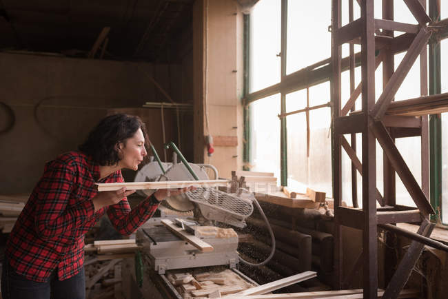 Woman bowling saw dust from plank in carpenter workshop — Stock Photo