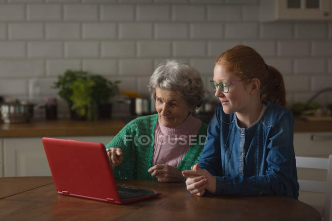 Großmutter und Enkelin nutzen Laptop in der heimischen Küche — Stockfoto