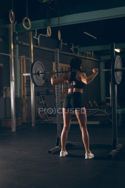 Visão traseira da mulher em forma levantando a barra no ginásio — Fotografia de Stock