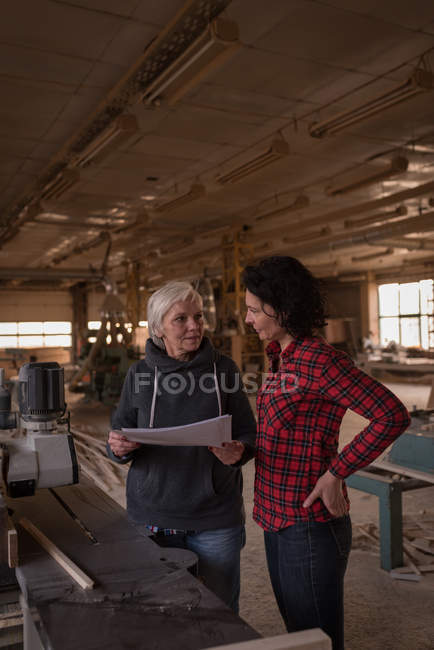 Mulheres discutindo sobre documentos em oficina de carpinteiro — Fotografia de Stock