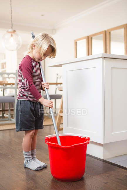 Мальчик держит швабру с ведром дома — стоковое фото