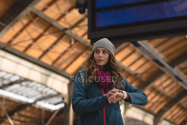 Mujer joven comprobando el tiempo en smartwatch en la estación de tren - foto de stock