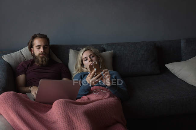 Мужчина использует ноутбук, а женщина использует мобильный телефон в гостиной дома — стоковое фото