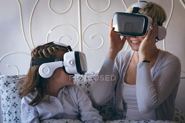 Mãe e filha usando fone de ouvido realidade virtual na cama em casa — Fotografia de Stock