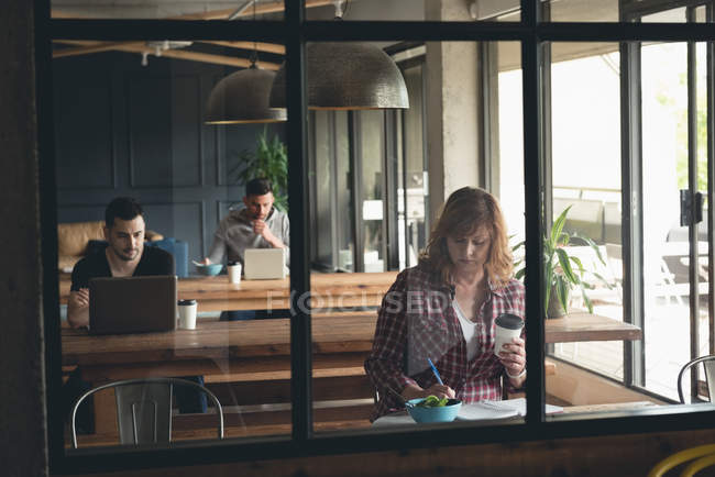 Empresária escrevendo em um diário na cafetaria no escritório — Fotografia de Stock