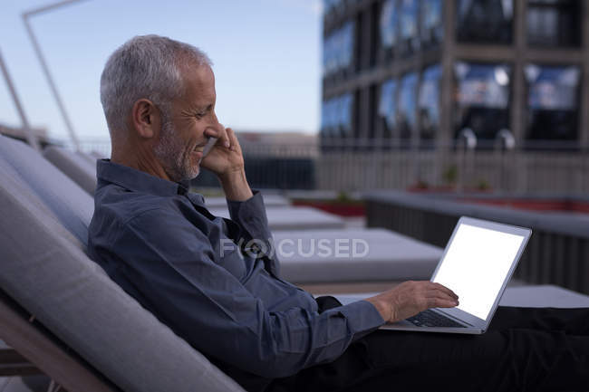 Empresário falando no celular enquanto trabalhava no laptop no hotel — Fotografia de Stock