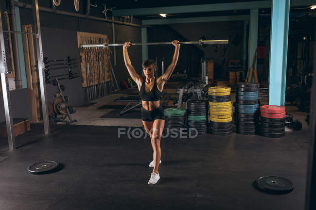 Fit femme soulevant la tige d'haltère dans la salle de gym — Photo de stock