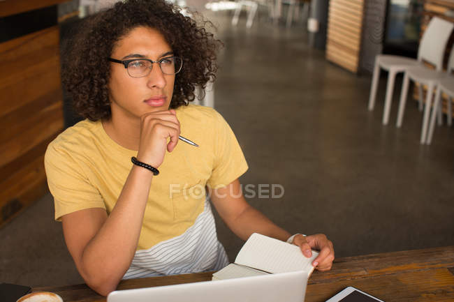 Thoughtful man writing on a diary in cafeteria — Stock Photo