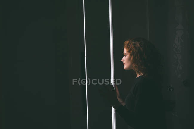 Задумчивая женщина смотрит в окно на дом — стоковое фото