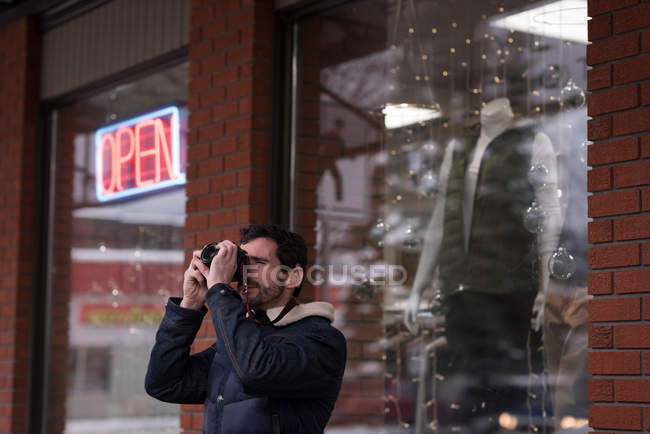 Hombre haciendo clic en la foto con cámara digital fuera de la tienda - foto de stock