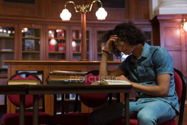 Молодий чоловік читає книгу в бібліотеці — стокове фото