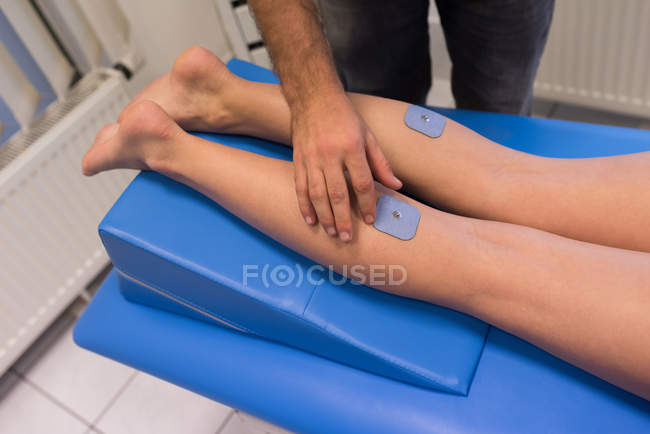 Fisioterapeuta colocando almohadillas en las piernas de la mujer en la clínica - foto de stock