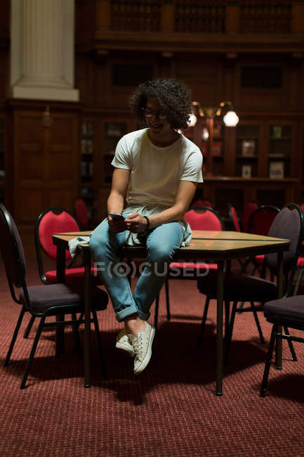 Молодий чоловік використовує мобільний телефон у бібліотеці — стокове фото