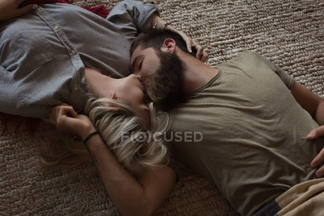 Casal beijando uns aos outros enquanto deitado na sala de estar em casa — Fotografia de Stock