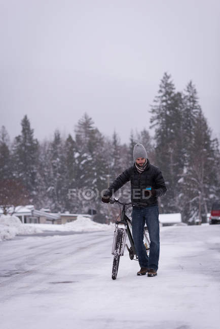 Uomo a piedi con la bicicletta sulla strada innevata durante l'inverno — Foto stock