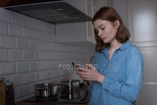 Молодая женщина с помощью мобильного телефона на кухне — стоковое фото