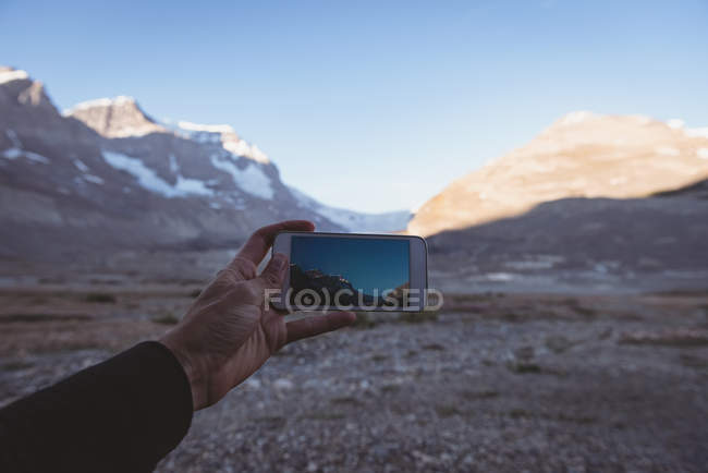 Homme prenant des photos de montagnes avec téléphone portable par une journée ensoleillée — Photo de stock