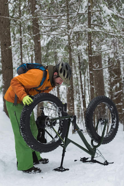 Hombre reparando su bicicleta en el bosque durante el invierno - foto de stock