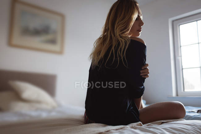 Mulher pensativa sentada na cama no quarto em casa — Fotografia de Stock