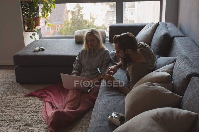 Couple utilisant ordinateur portable et tablette numérique dans le salon à la maison — Photo de stock