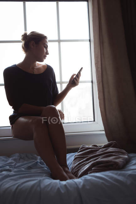 Femme utilisant un téléphone portable près de la fenêtre à la maison — Photo de stock